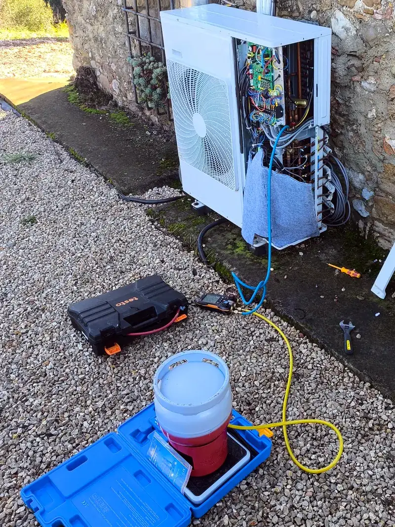 Unidad exterior abierta con manómetros y báscula durante la carga de gas tras una reparación